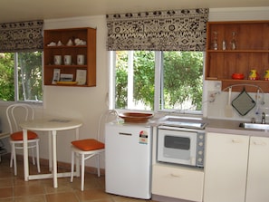A compact kitchen with a refrigerator, microwave, and a small dining area with two chairs. - Lovely 1-bedroom studio in Russell perfect for a relaxing getaway (Russell)