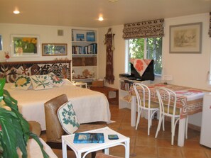 Een slaapkamer met een bed, nachtkastje en een bureau met stoelen. Er staan boekenkasten en een raam met uitzicht.