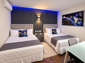 A hotel room with two beds, a desk, and a wall-mounted air conditioner.