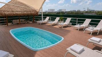 A rooftop pool area with lounge chairs and a thatched umbrella.