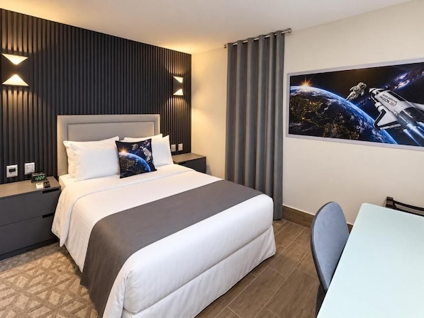 Una habitación de hotel con una cama, mesitas de noche, un escritorio y una silla.
