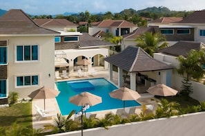 Una zona residenziale con piscina circondata da lettini e ombrelloni, con case sullo sfondo.