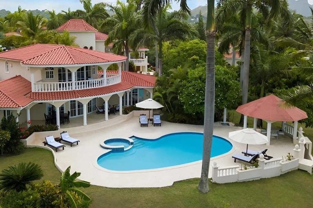Une grande maison avec une piscine, entourée de palmiers et d’une pelouse bien entretenue.