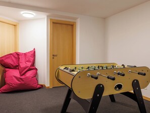 Ein Zimmer mit einem Tischkicker, einem roten Sitzsack und einer Holztür.