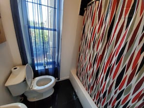 A bathroom with a toilet, a window with curtains, and a shower area with a patterned curtain.