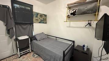 Une petite chambre à coucher, bien rangée, avec un lit simple, une table de chevet, une télévision et une étagère avec des serviettes.