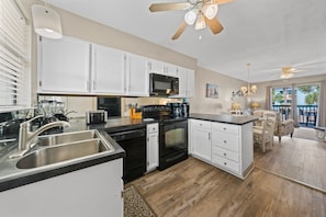A modern kitchen with white cabinets, stainless steel appliances, and a wooden floor. - Quaint Getaway With Pool and Beach Access (Gulf Shores)