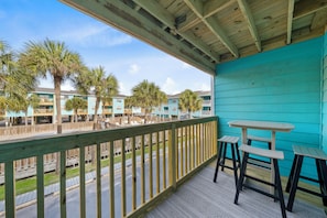 A balcony with a wooden railing, a table, and two chairs. - Quaint Getaway With Pool and Beach Access (Gulf Shores)