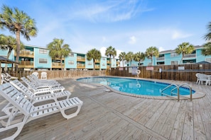 A pool area with lounge chairs, a wooden deck, and a building with balconies. - Quaint Getaway With Pool and Beach Access (Gulf Shores)