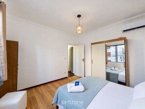 A hotel room with a bed, a wooden floor, a hanging light fixture, a wardrobe, and an air conditioning unit. - Condo. Apt. 890m From the Beach Mil0011 (Salvador)