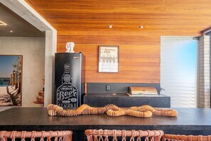 A modern kitchen with a wooden ceiling, a black refrigerator, a framed Beatles poster, and a grill on the counter. - Apt. w/ Ocean View in Condo. w/ Pool Mle0201 (Camaçari)