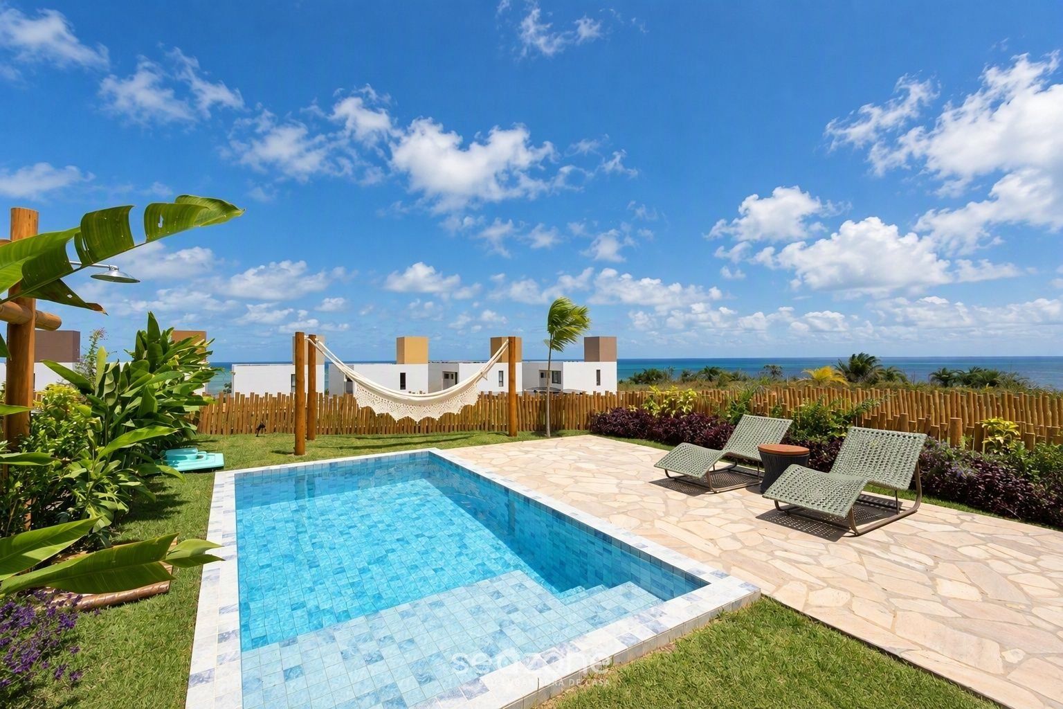 A swimming pool with a hammock, lounge chairs, and a view of the ocean.