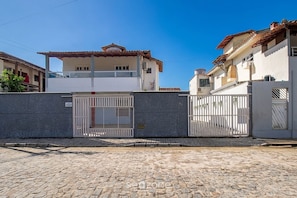 A cobblestone street with a gated entrance, a two-story building with a tiled roof, and a white fence. - Apt. in Condo. w/ Pool & BBQ Pax0005 (Porto Seguro)