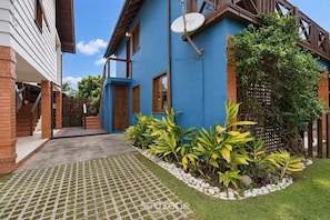 Ein Wohnhaus mit blauer Fassade, einer Satellitenschüssel, einem verschlossenen Eingangstor und einem gepflegten Garten mit verschiedenen Pflanzen.