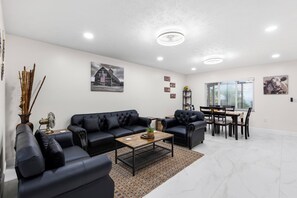 A modern living room with a black leather sofa, a coffee table, and a dining area with a wooden table and chairs. - Charming 3-bedroom house in tranquil Dade City with AC (Dade City)