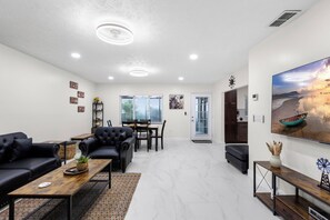 A modern living room with a black leather sofa, a wooden coffee table, and a dining area with a table and chairs. - Charming 3-bedroom house in tranquil Dade City with AC (Dade City)