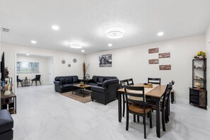 A modern living room with a dining area, featuring a black leather sofa, a wooden dining table, and a chandelier. - Charming 3-bedroom house in tranquil Dade City with AC (Dade City)