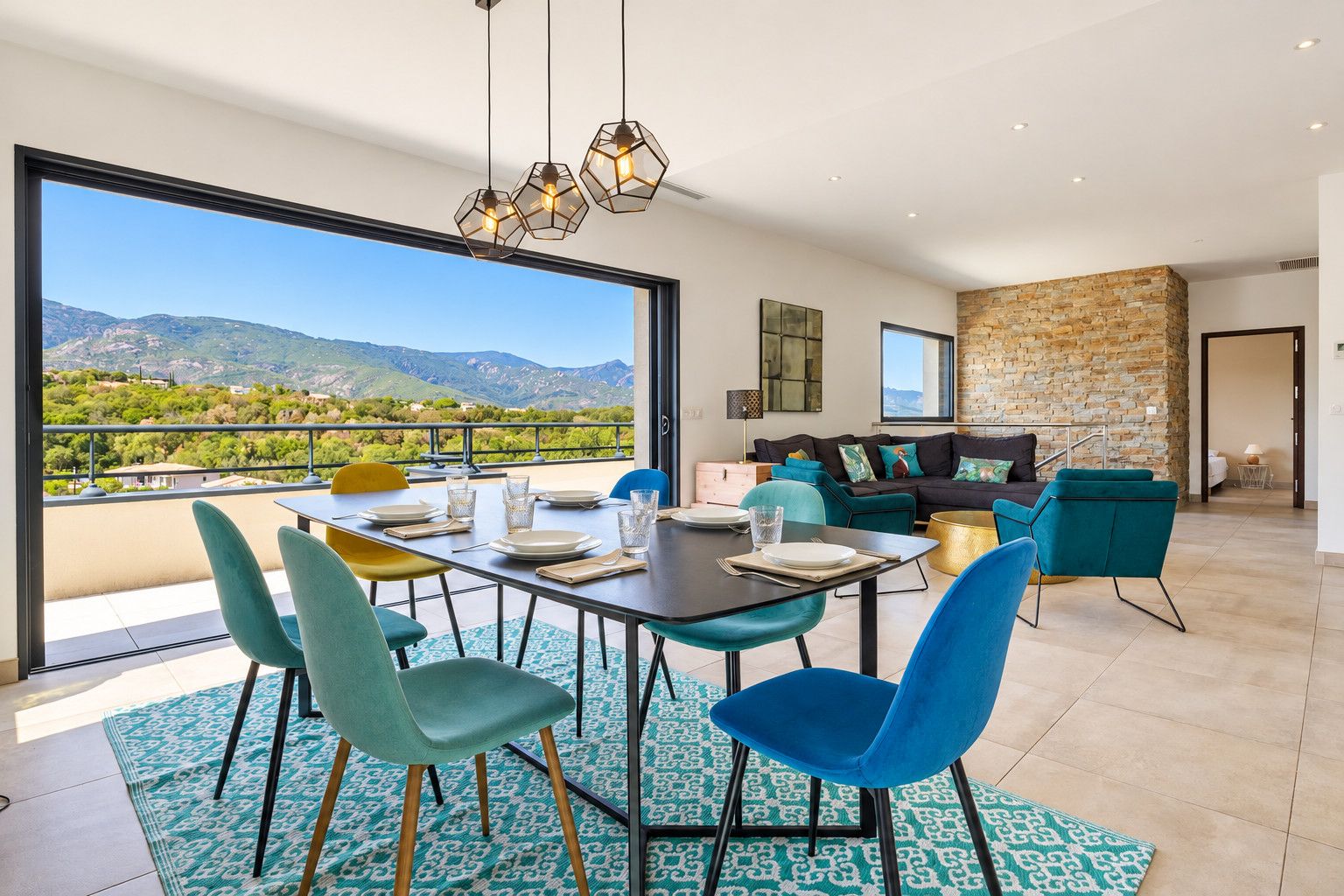 A modern living room with a dining area, a stone wall, and a view of mountains.