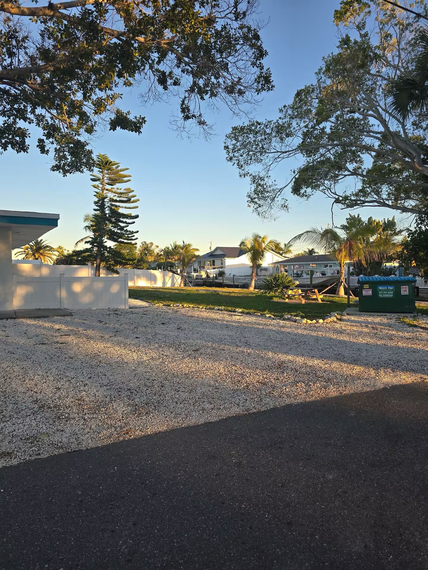 A residential area with a gravel driveway, a white building, and a house with a dark roof.