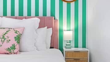 Een bed met witte beddengoed en meerdere kussens, een nachtkastje met een lamp, en een muur met verticale strepen.
