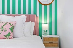 Un lit avec une literie blanche et plusieurs oreillers, une table de chevet avec une lampe, et un mur à rayures verticales.