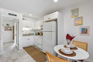 Une cuisine moderne avec des meubles blancs, un réfrigérateur et un coin repas avec une table mise pour deux personnes.