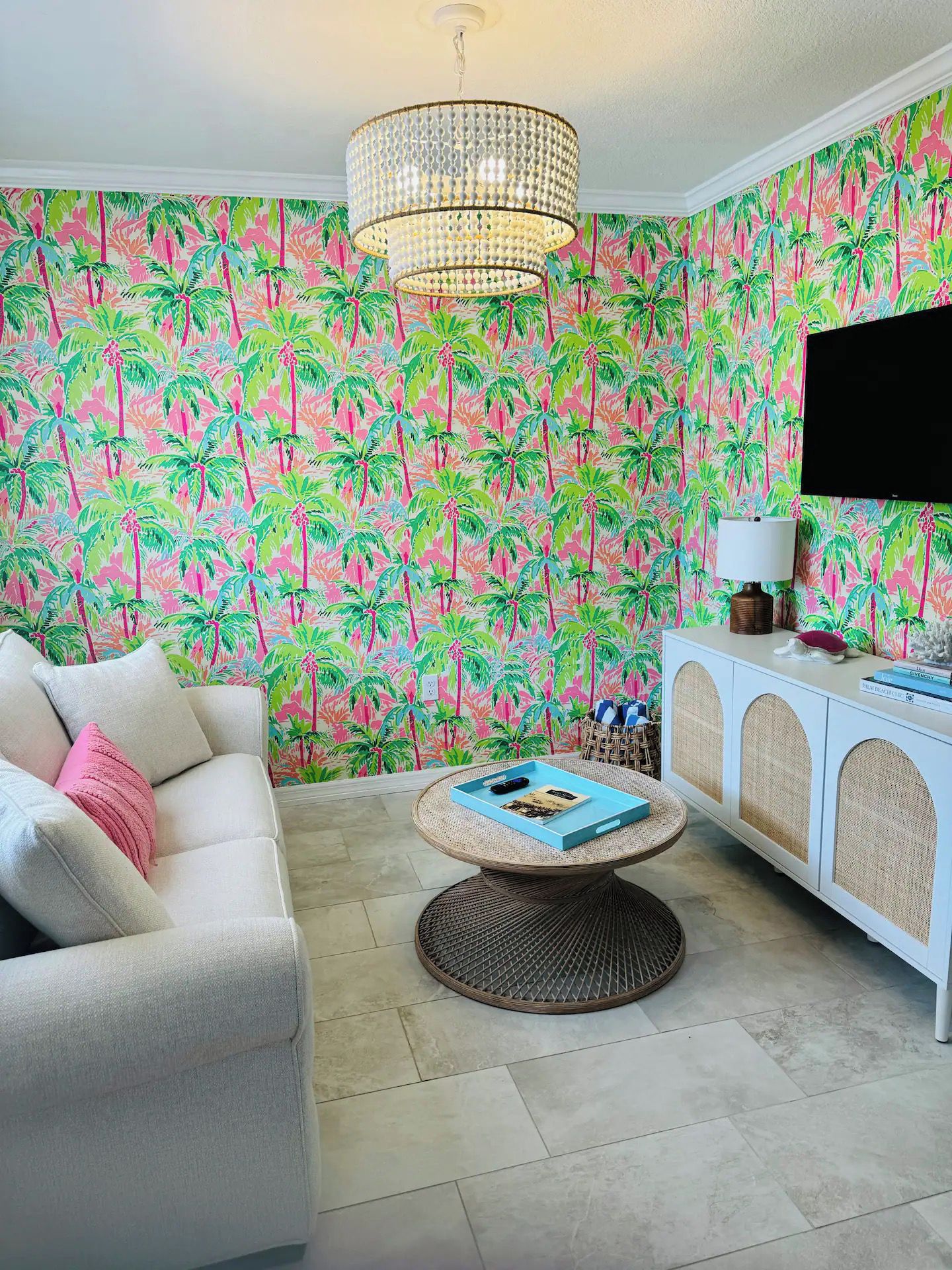 Een woonkamer met behang met een patroon, een witte bank, een ronde salontafel en een televisietoestel op een meubel.