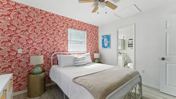 A bedroom with a bed, a bedside table, a lamp, a window with blinds, a ceiling fan, and a door.