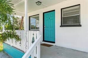 Une maison avec une porte de couleur turquoise, des murs extérieurs blancs et un porche doté d’une balustrade blanche.