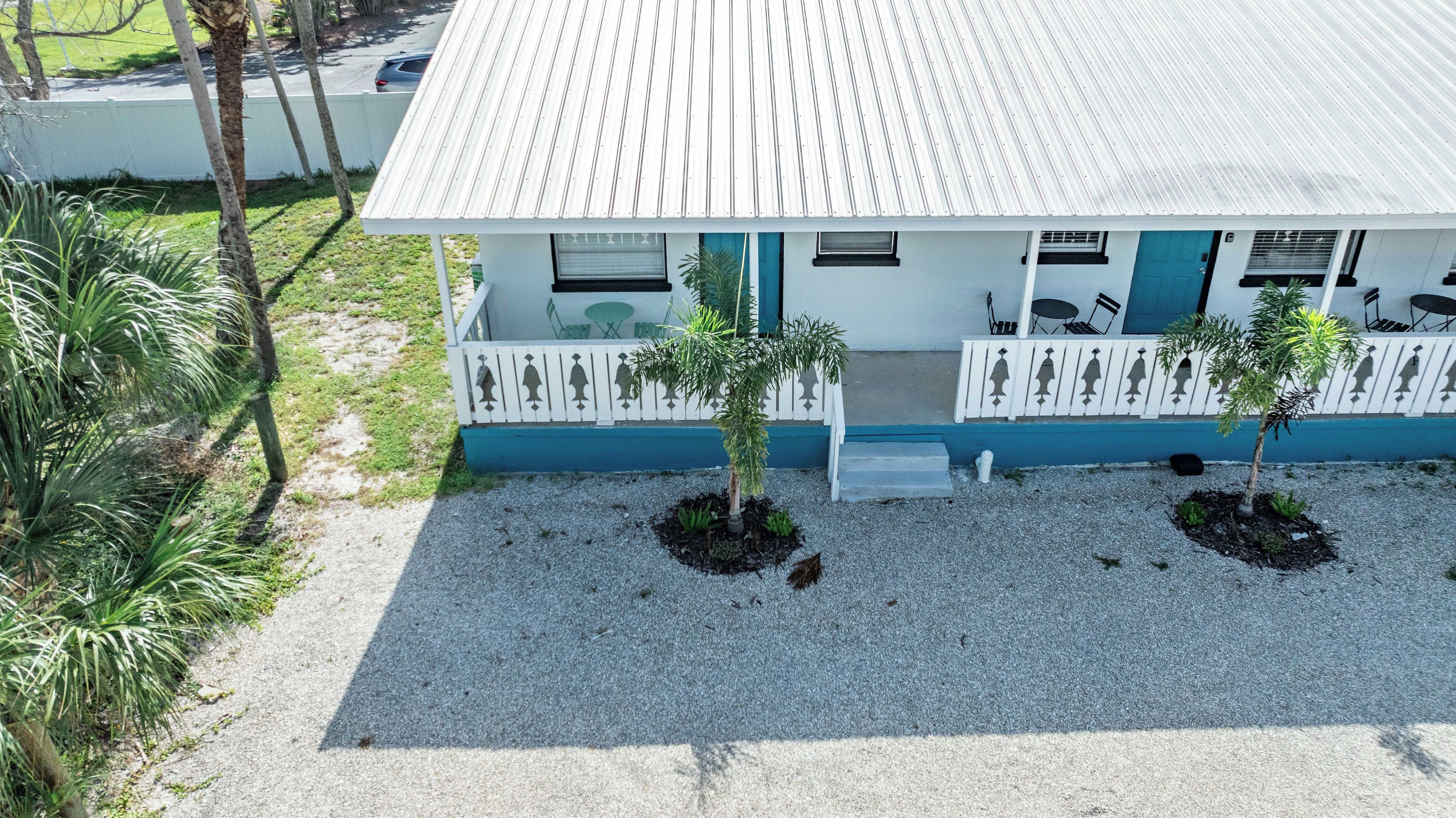 A two-story building with a white exterior and blue accents, featuring a covered porch with outdoor seating and two small trees.