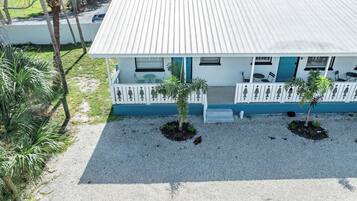 A two-story building with a white exterior and blue accents, featuring a covered porch with outdoor seating and two small trees.