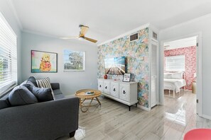 Un salon avec un canapé gris, une table ronde en osier et un meuble blanc orné d’un papier peint à motifs floraux.