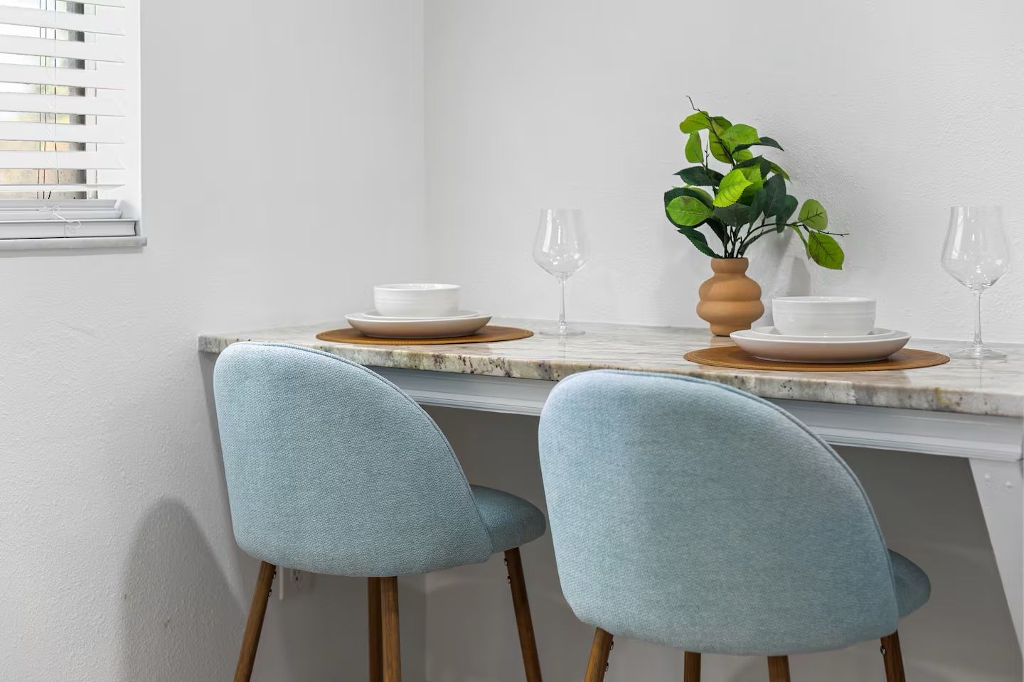 A dining area with two light blue chairs, a marble table, white plates, and a potted plant.