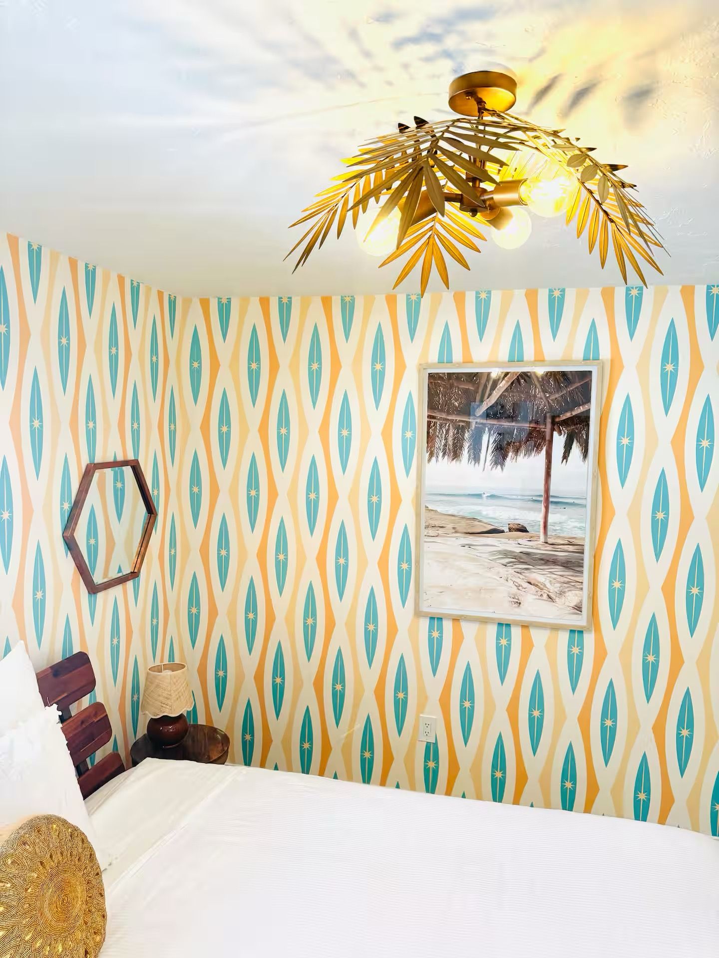 A room with a patterned wallpaper, a bed, a framed picture, and a unique ceiling light fixture.