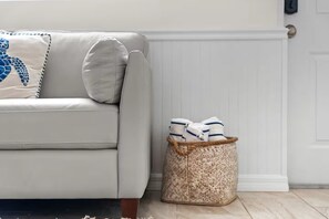Un canapé de couleur claire, agrémenté d’un coussin décoratif et d’un panier en osier contenant des serviettes pliées.