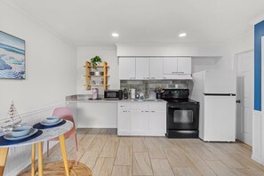 Une cuisine de taille réduite avec des meubles blancs, une cuisinière noire et un réfrigérateur blanc.