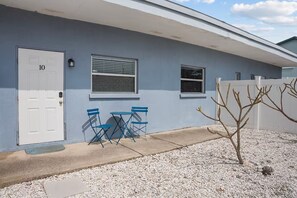 Un bâtiment avec une porte blanche portant le numéro 10, deux fenêtres et un petit patio aménagé avec des chaises pliantes bleues.