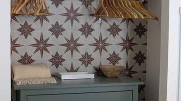 Une pièce avec un mur orné de motifs, un bol en bois, un plaid beige et une boîte blanche posée sur une commode verte.