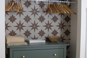 Une pièce avec un mur orné de motifs, un bol en bois, un plaid beige et une boîte blanche posée sur une commode verte.