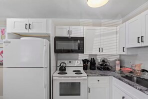 Une cuisine moderne avec des meubles blancs, un micro-ondes noir, une cuisinière blanche et un évier en acier inoxydable.