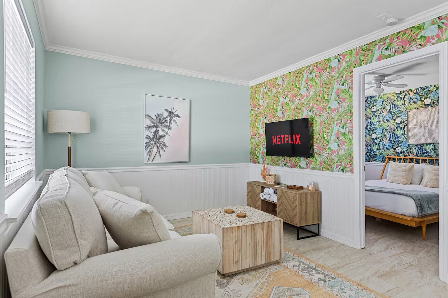 Una sala de estar con sofá, mesa de centro, televisor montado en la pared y cama con cabecera.