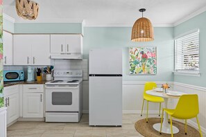 Une cuisine avec des meubles blancs, une cuisinière, un four à micro-ondes et un réfrigérateur. On y trouve également un coin repas avec une table et deux chaises.