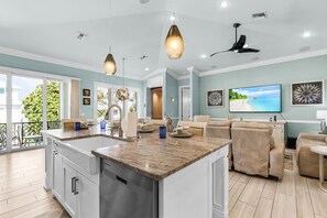 A modern kitchen with a central island, dining area with chairs, a ceiling fan, and a large TV on the wall. - Family-Friendly Retreat in Prime Carolina Location (Fort Myers Beach)