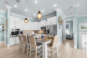 A modern kitchen with white cabinetry, stainless steel appliances, and a central island with chairs. - Family-Friendly Retreat in Prime Carolina Location (Fort Myers Beach)