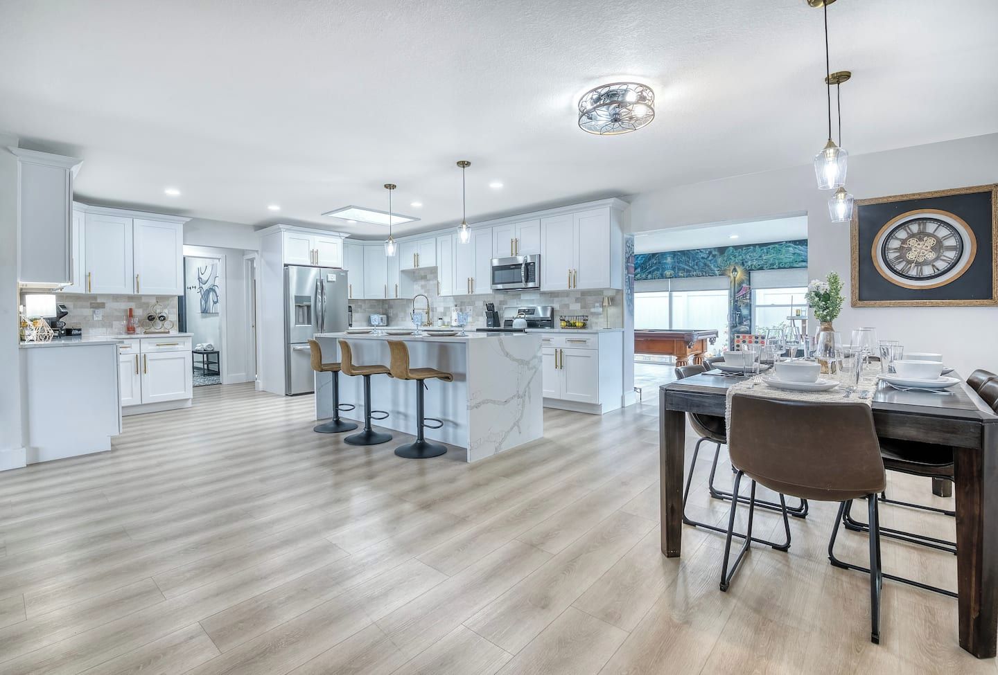 A modern kitchen with white cabinetry, a central island with bar stools, and a dining area with a dark wood table and chairs.