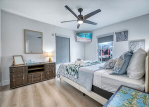 Un dormitorio con cama, cómoda, ventilador de techo, ventana y obras de arte en las paredes.