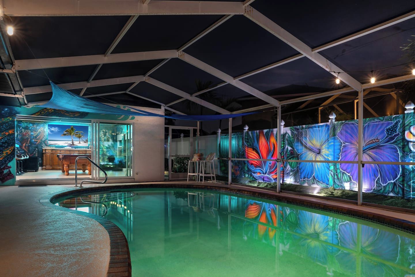 An indoor swimming pool with a glass wall featuring a colorful butterfly mural, a poolside seating area, and a covered patio.