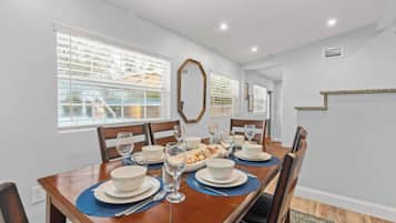 A dining area with a wooden table set for four, surrounded by chairs.
