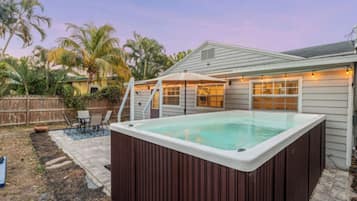 A backyard with a hot tub, patio furniture, and a wooden fence.
