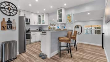 A modern kitchen with white cabinetry, a central island with bar stools, a stainless steel refrigerator, and a clock on the wall.